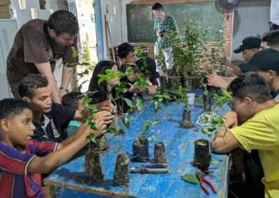 A group of children of various ages is gathered around a table with various plant sprouts that they are observing and touching