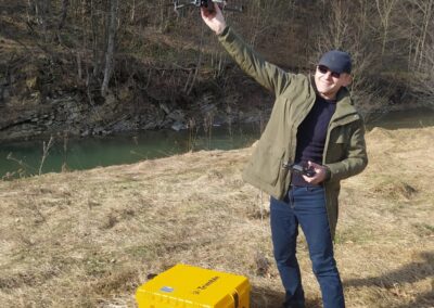 A smiling man is holding a drone overhead, ready to launch, with controls in his other hand