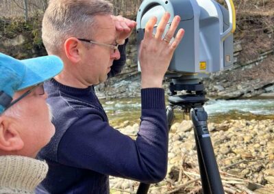 Two men operating survey equipment, with one looking through the device across a river